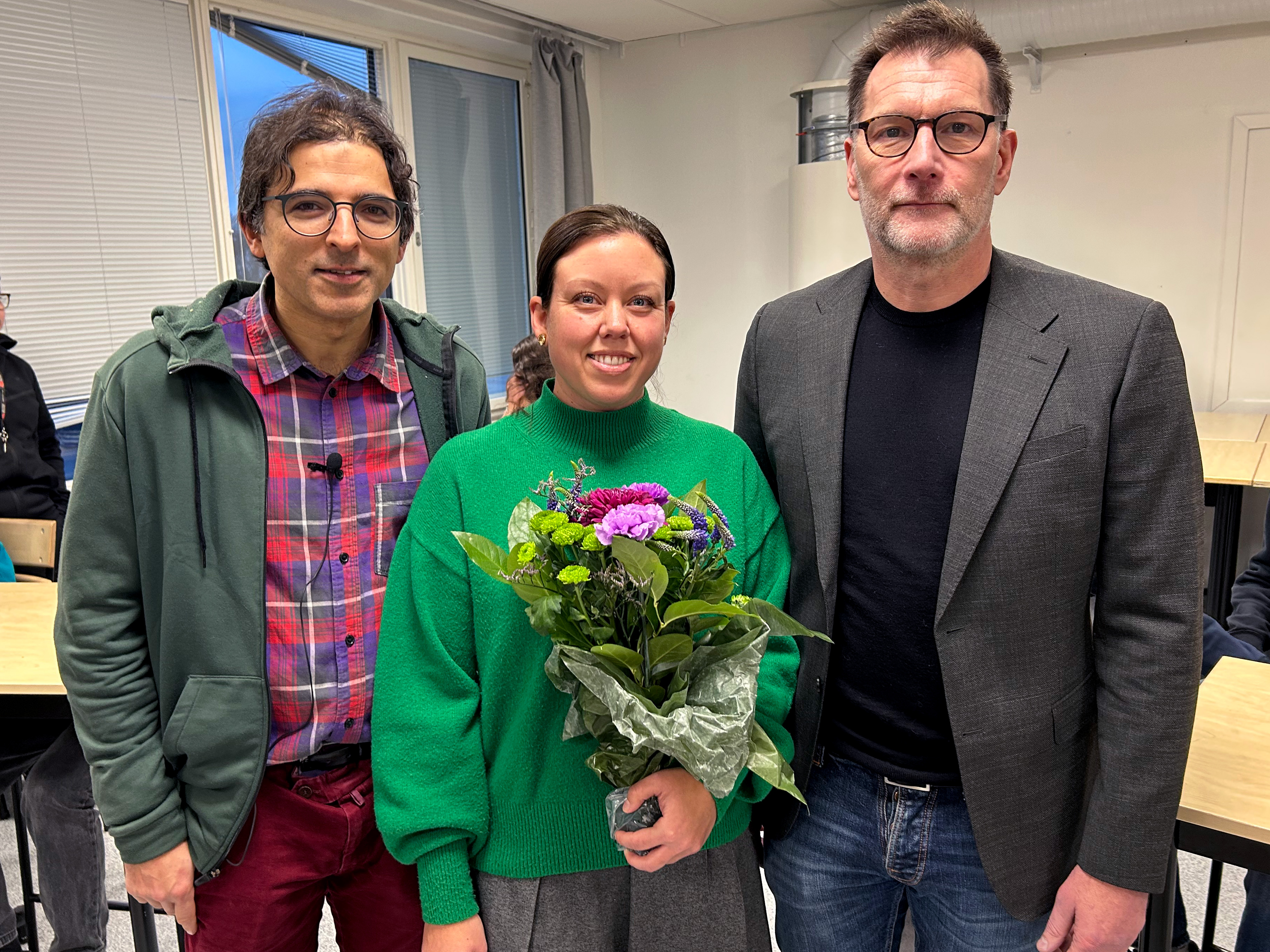 Olof Oskarsson, verksamhetsområdeschef för kommunala grundskolan, som räcker över en stor blombukett till Emelie Hahn, och Tarik Qureshi, grundskoleutskottets ordförande (V) 